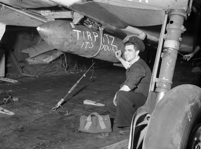 Abbildung 3: Beschriftung einer Bombe auf dem britischen Flugzeugträger HMS Furious am 3.4.1944 in Vorbereitung des Angriffs auf das deutsche Schlachtschiff Tirpitz (Quelle: F.A. Hudson, Royal Navy officialphotographer/Wikmedia, https://commons.wikimedia.org/wiki/File:HMS_Furious_armourer_with_bomb_message_April_1944_IWM_A_22640.jpg)